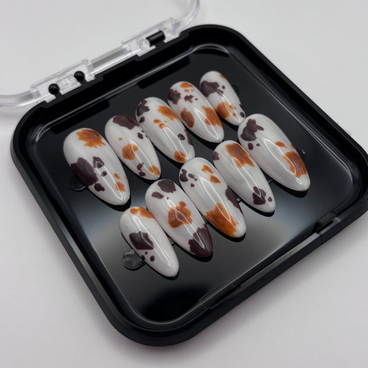 Extensions de faux ongles Sienna en motif vache, press-on de la marque Onailsbymanon, visibles dans cette image.